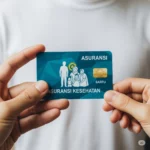 Tangan memegang kartu asuransi kesehatan dengan latar belakang keluarga terlindungi, melambangkan pentingnya asuransi.